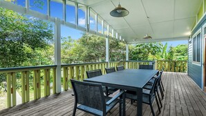 A covered outdoor patio with a table and chairs, surrounded by a wooden deck and a railing.