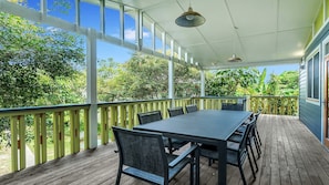 A covered outdoor patio with a table and chairs, surrounded by a wooden deck and a railing.