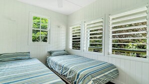 Une chambre avec deux lits, des murs blancs et une fenêtre avec des volets.