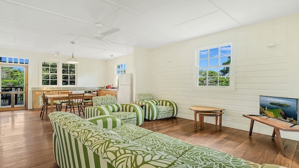 A spacious living area with a long green-striped sofa, a wooden dining table, and a TV on a wooden stand.