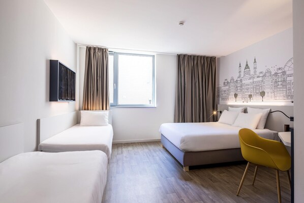 Quarto de hotel com duas camas de solteiro, uma escrivaninha, uma cadeira, uma janela com cortinas e um mural na parede.