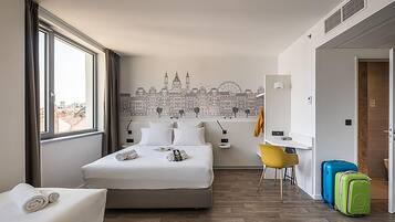 Quarto de hotel com uma cama, uma escrivaninha, uma cadeira e duas malas.
