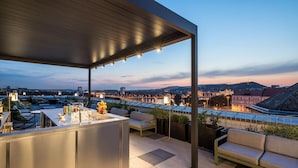 Un bar en la azotea con vista a un paisaje urbano al anochecer.