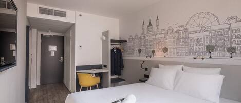 A hotel room with a bed, a desk, a chair, and a wall mural of a cityscape.