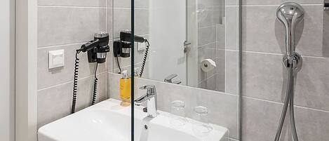 A modern bathroom with a glass shower enclosure, a white sink, and a hairdryer on the wall.