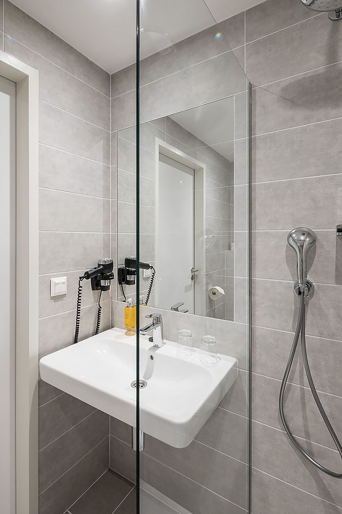 A modern bathroom with a glass shower enclosure, a white sink, and a hairdryer on the wall.