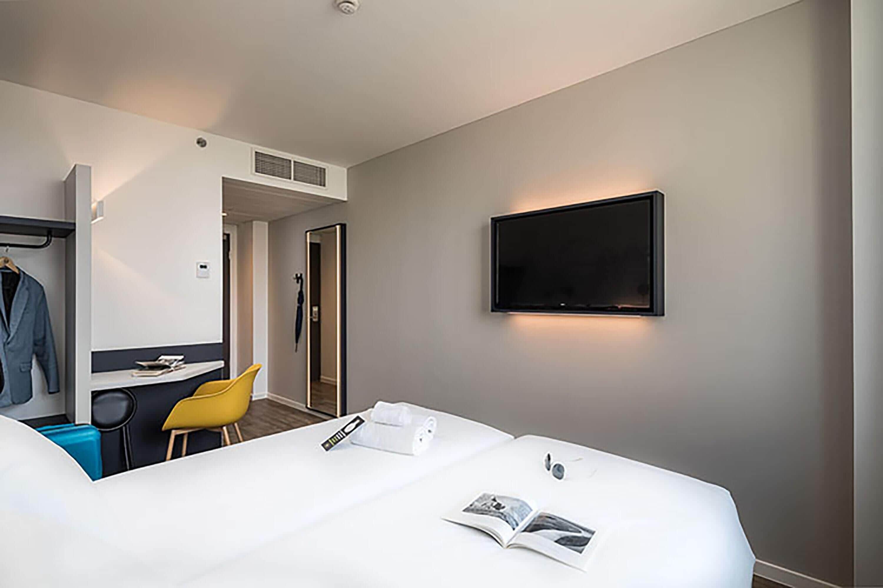 Ein Hotelzimmer mit Bett, Schreibtisch, Stuhl, Fernseher und Kleiderschrank.