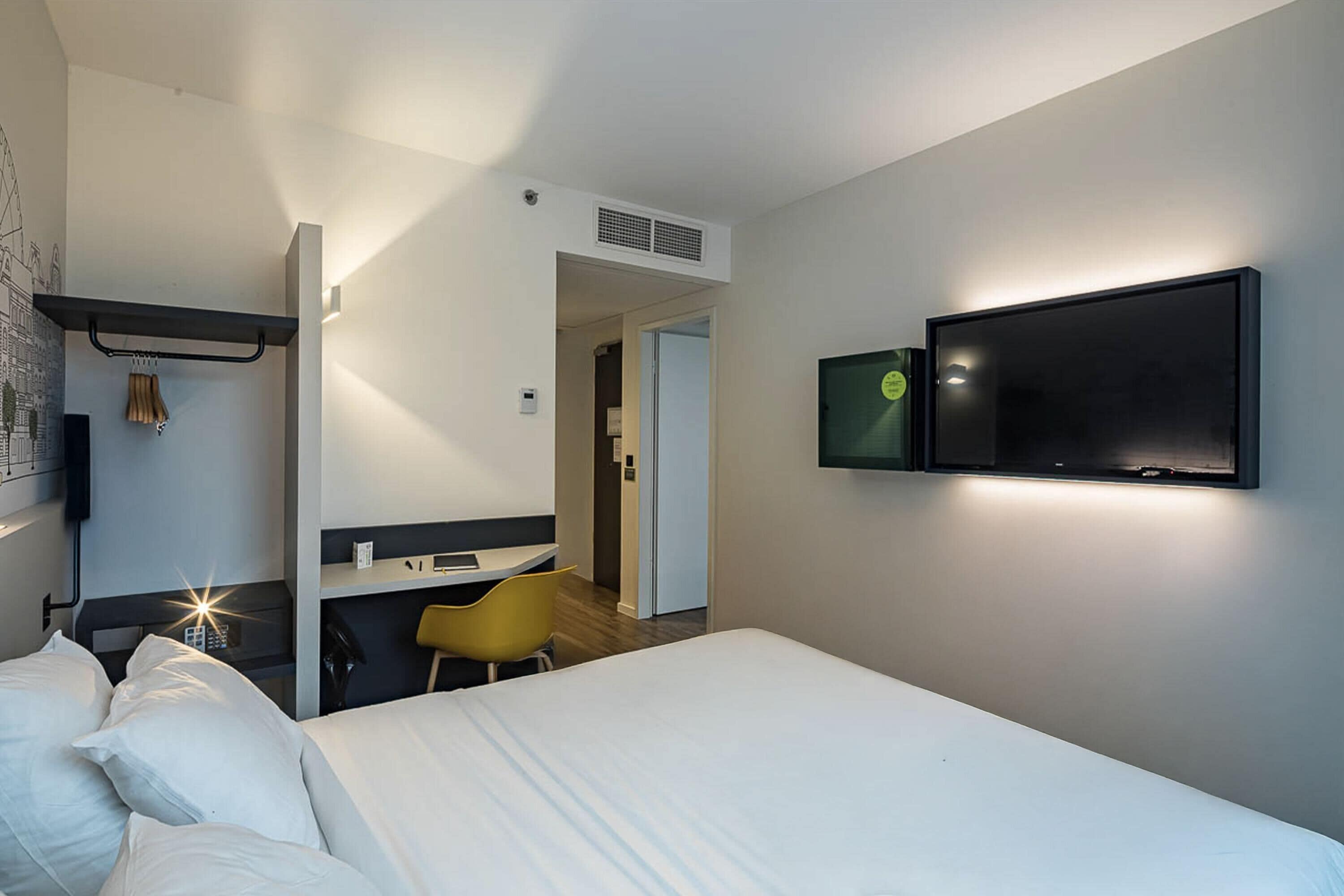Una habitación de hotel con cama, escritorio, silla, televisor y armario.