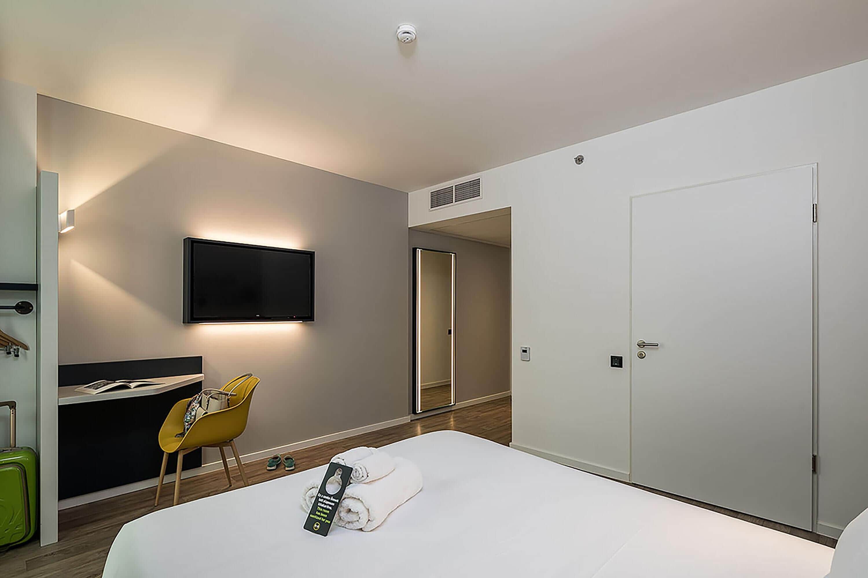 A hotel room with a bed, a desk, a chair, a TV, and a wardrobe.