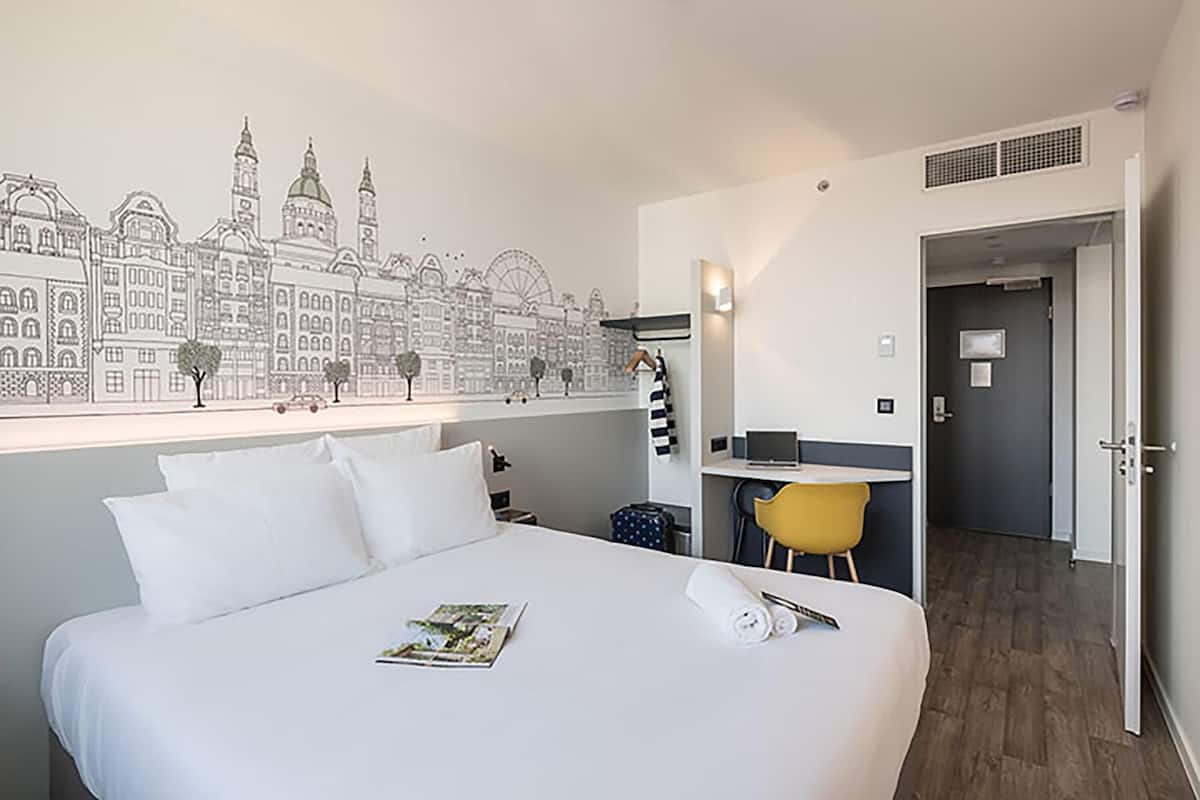 A hotel room with a large bed, a desk, a chair, and a wall mural.