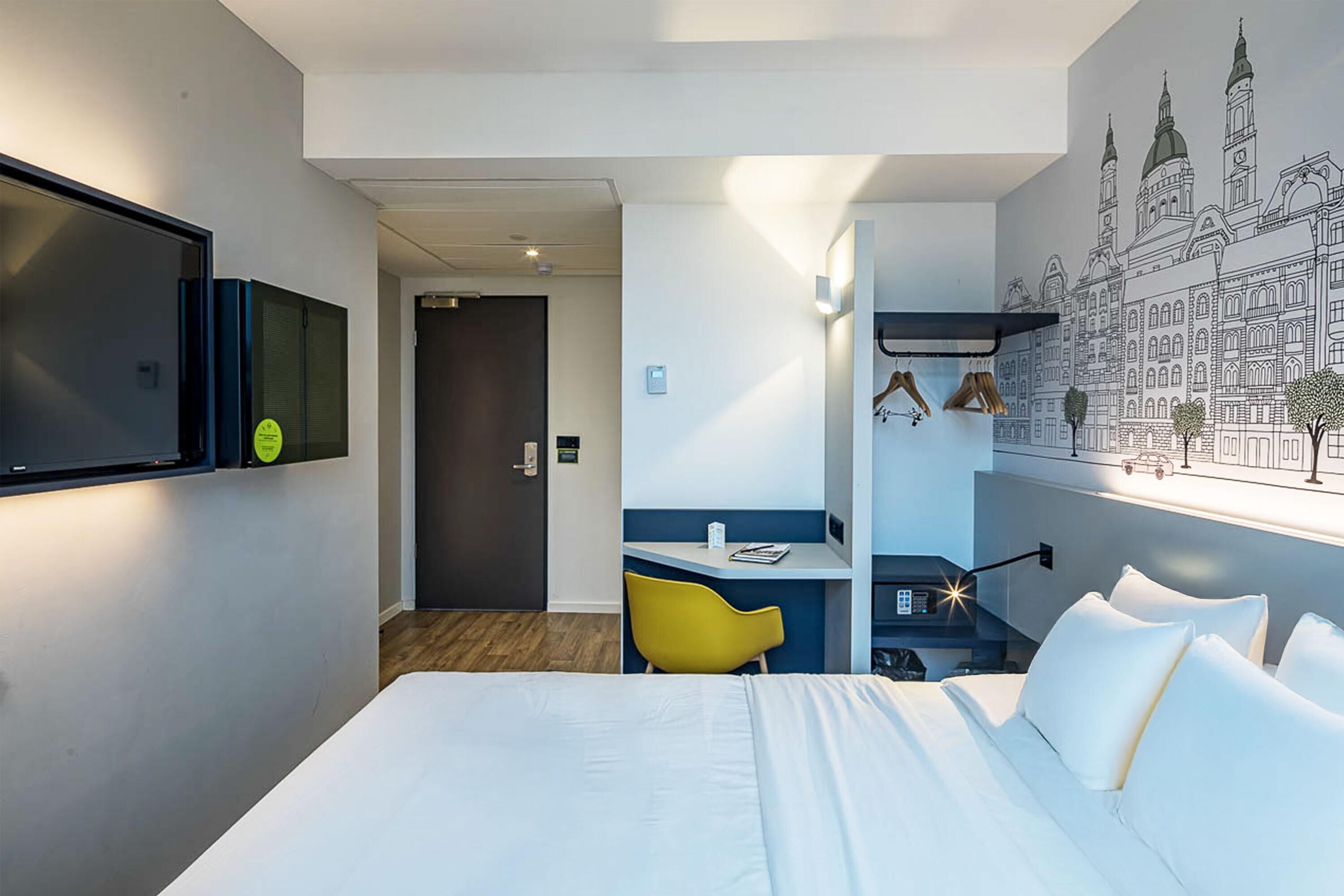 Habitación de hotel con cama, escritorio, silla y televisor montado en la pared.