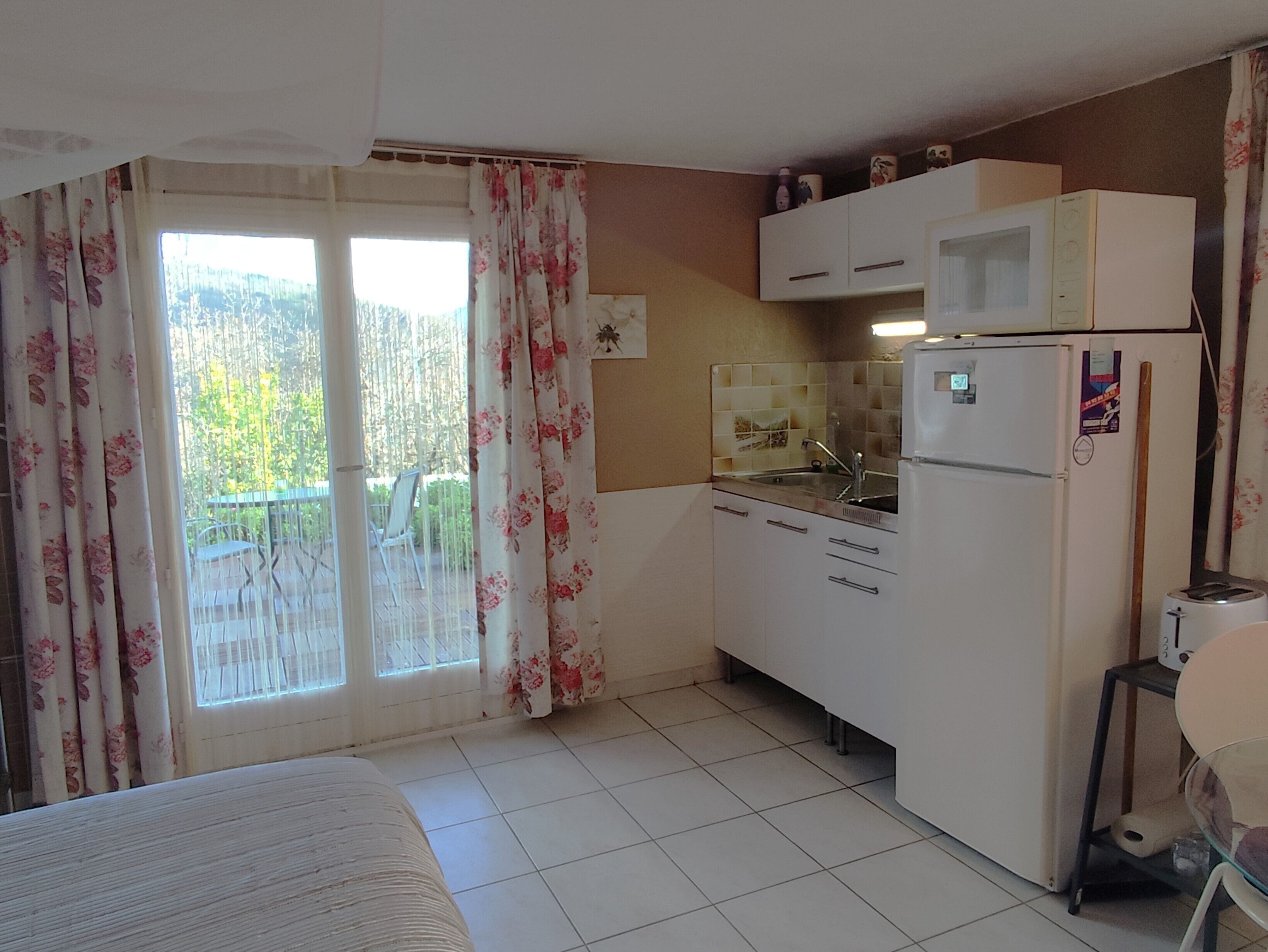 A compact kitchen with a refrigerator, microwave, and sink. There's a balcony with a view of greenery.