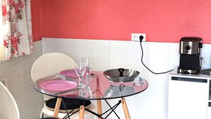 A dining area with a glass table set for two, a coffee maker, and a power outlet on the wall. - Studio (Bendejun)