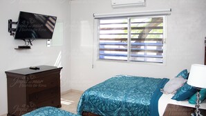 Een slaapkamer met een bed, een dressoir, een televisie en een raam met zonwering.