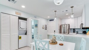 Una cocina moderna con armarios blancos, un refrigerador de acero inoxidable y una zona de comedor con una mesa blanca y sillas turquesa.