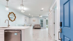 Una cocina moderna con una isla central, un comedor con sillas, un sofá y una puerta azul.