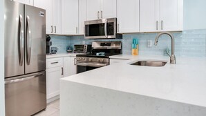 Una cocina moderna con armarios blancos, electrodomésticos de acero inoxidable, un microondas, horno y un lavamanos con grifo.