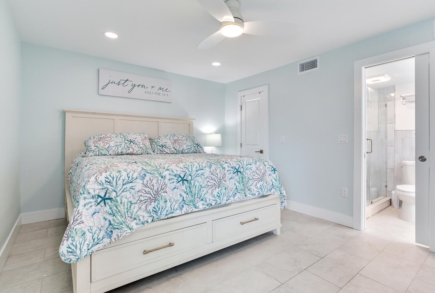A bedroom with a bed, a ceiling fan, a nightstand, and a door leading to a bathroom.
