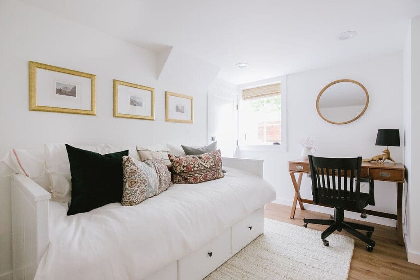 A bedroom with a white bed, a desk, and a chair. There are three framed pictures on the wall.