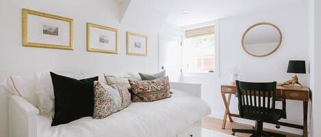 A bedroom with a white bed, a desk, and a chair. There are three framed pictures on the wall.