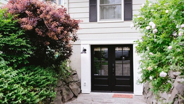 A house with a black front door, a small porch, and a stone wall.