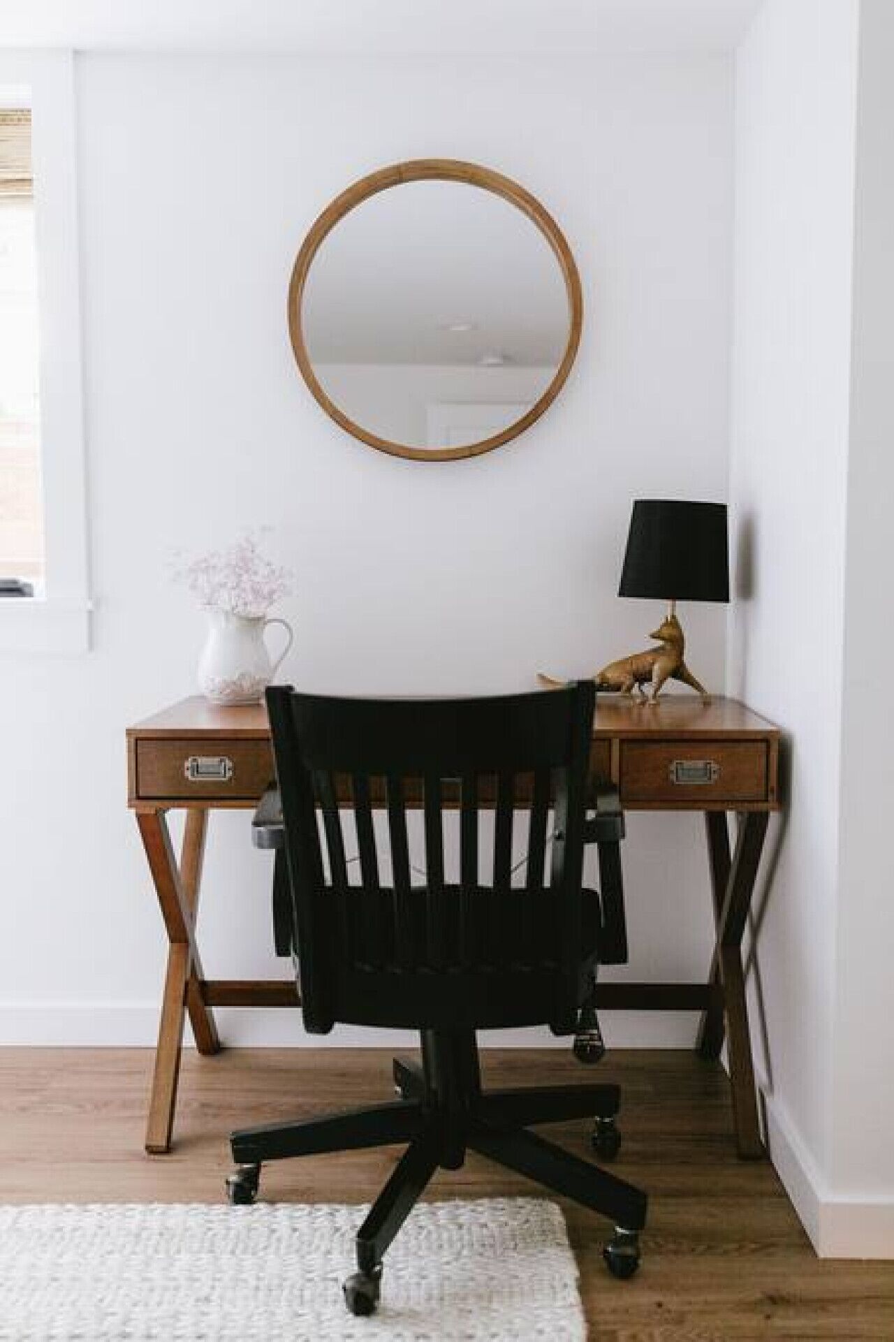 A wooden desk with a round mirror, a lamp, and a small figurine.
