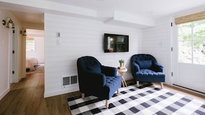 A room with two dark blue armchairs, a black and white checkered rug, and a television mounted on the wall.