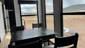 Un comedor moderno con un amplio ventanal que ofrece vistas a un campo de hierba y colinas distantes.