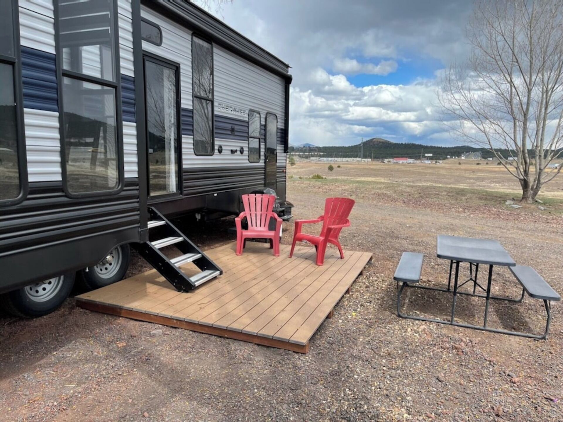 A mobile home with a deck, two red Adirondack chairs, and a picnic table.