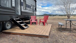 Una autocaravana con una rampa que lleva a una terraza con dos sillas y una mesa.