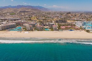 A coastal resort with multiple hotel buildings, a sandy beach, and a clear view of the ocean.