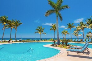 A pool area with lounge chairs and palm trees, overlooking a clear blue sky and ocean.