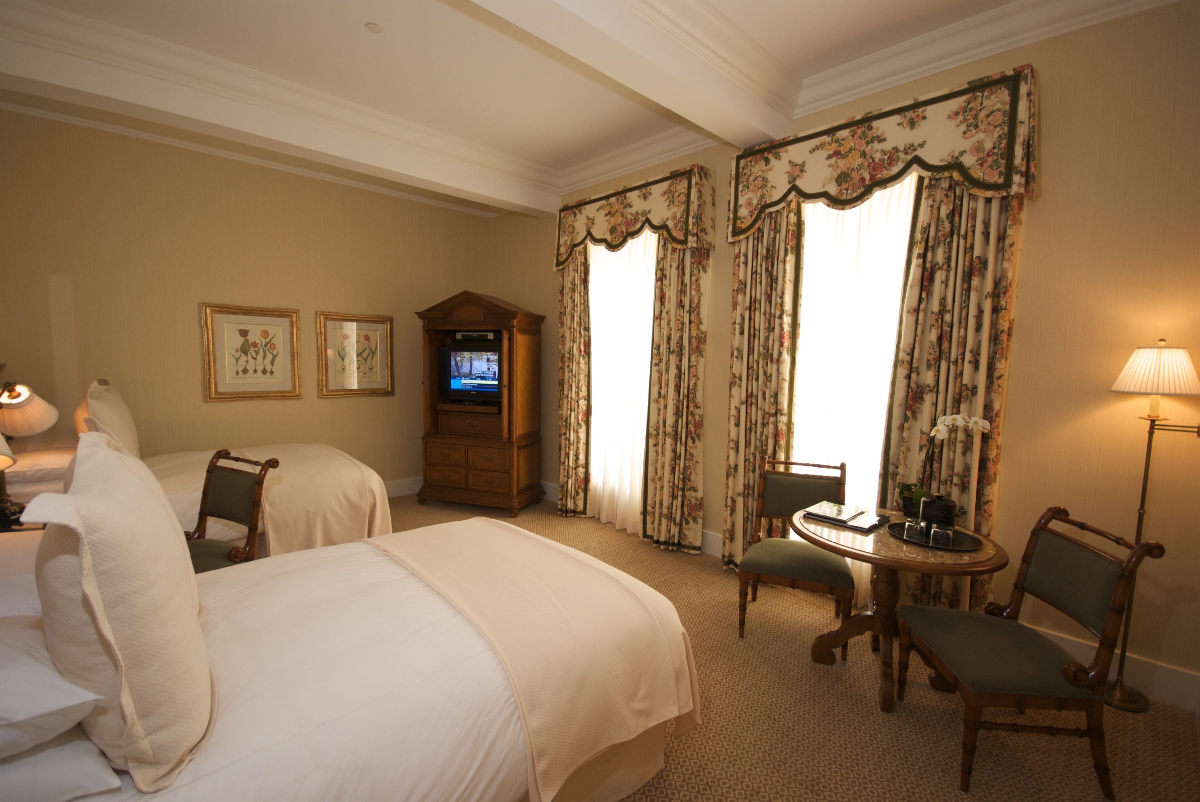 A hotel room with two beds, a television, a desk with a chair, and a lamp.