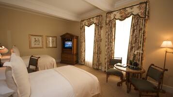A hotel room with two beds, a television, a desk with a chair, and a lamp.