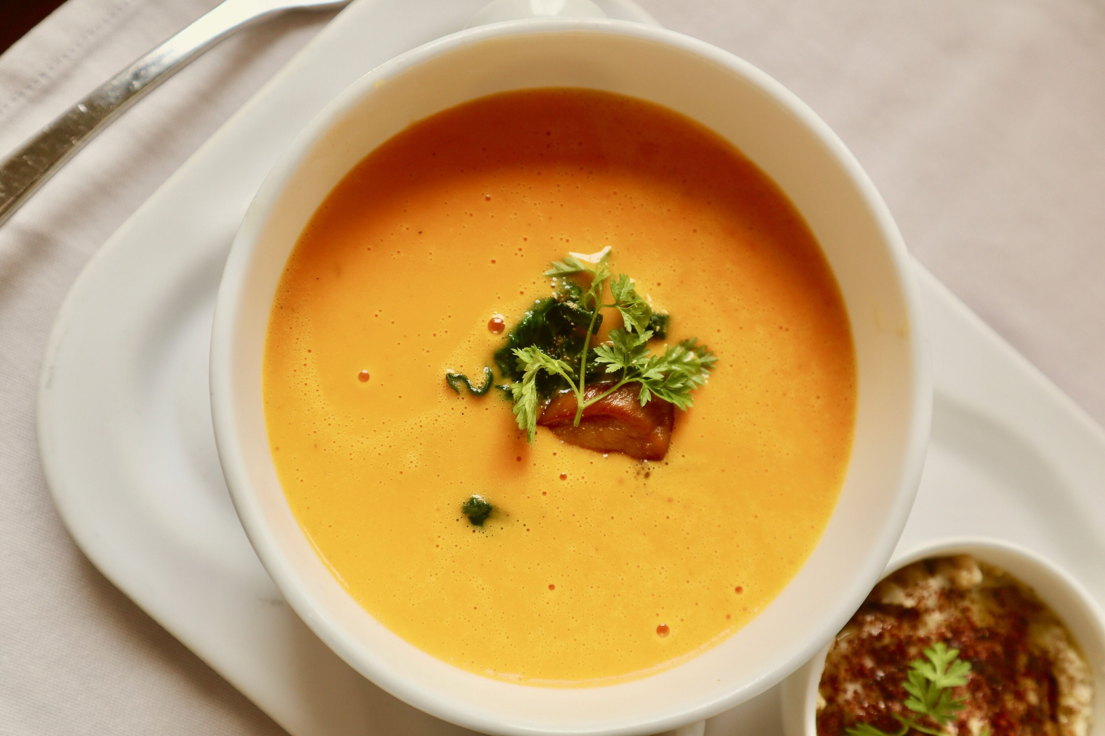 A bowl of soup with a garnish on a white plate.
