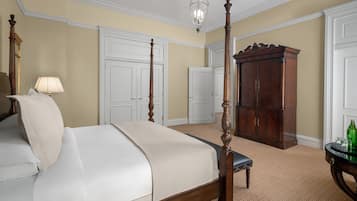 A four-poster bed with a wooden frame, a bedside table with a lamp, and a large wooden cabinet in a room with beige walls and patterned carpet.