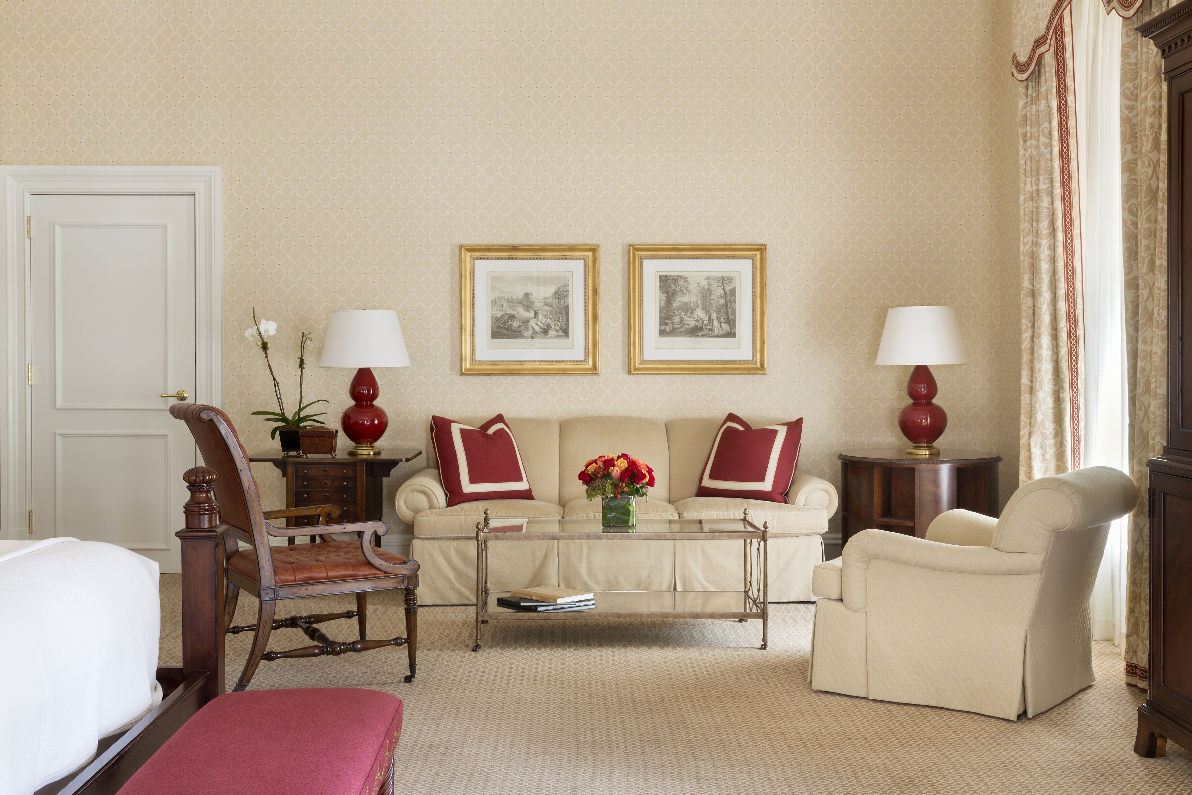 Sala de estar con sofá, sillones, una mesa de centro y dos lámparas. Se observan dos cuadros en la pared y una puerta a la izquierda.