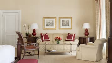 Sala de estar con sofá, sillones, una mesa de centro y dos lámparas. Se observan dos cuadros en la pared y una puerta a la izquierda.
