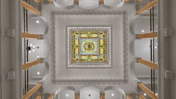 A grand atrium with a central stained glass window, white columns, and a chandelier.