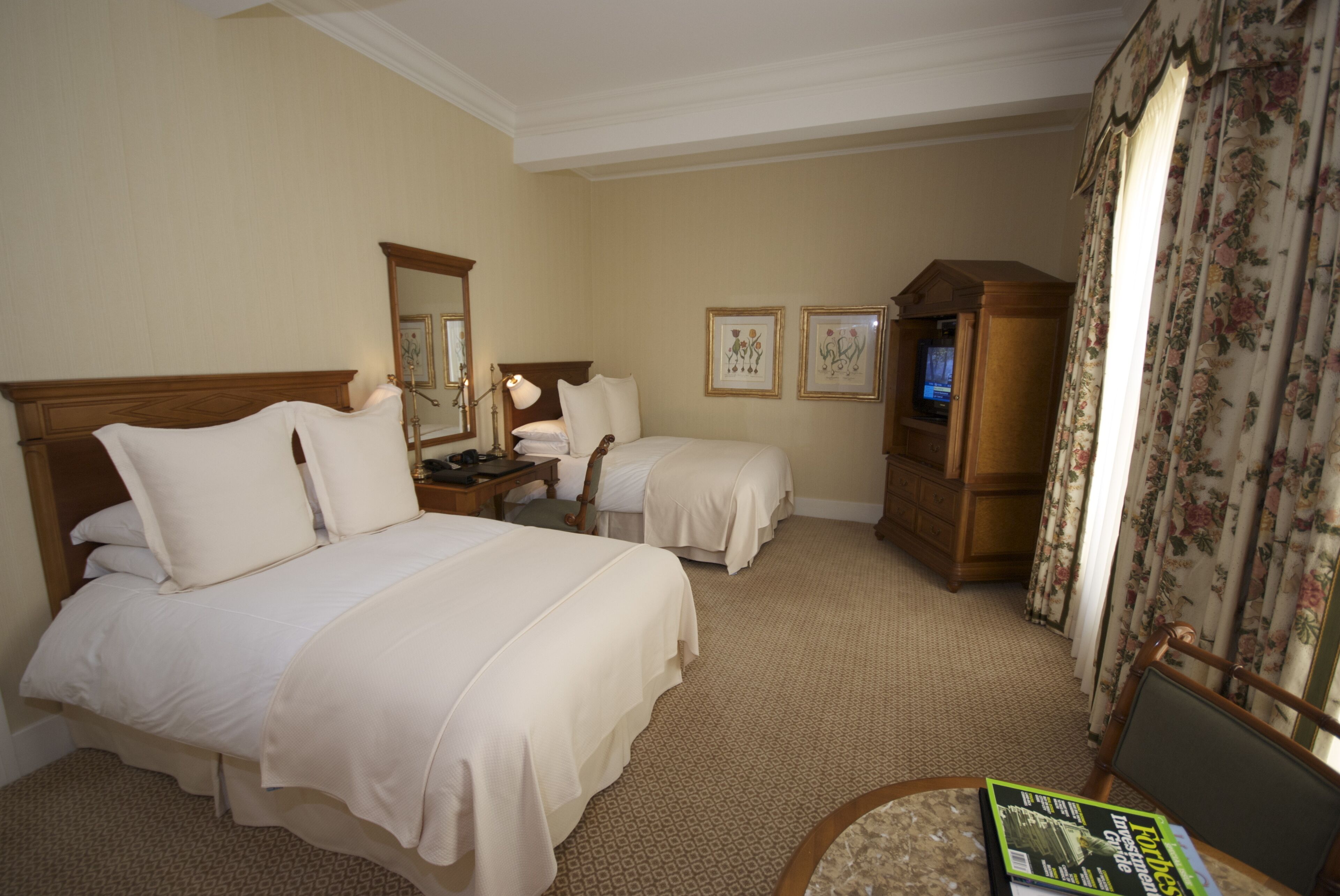 Una habitación de hotel con dos camas, un escritorio, una silla, un televisor y un espejo.