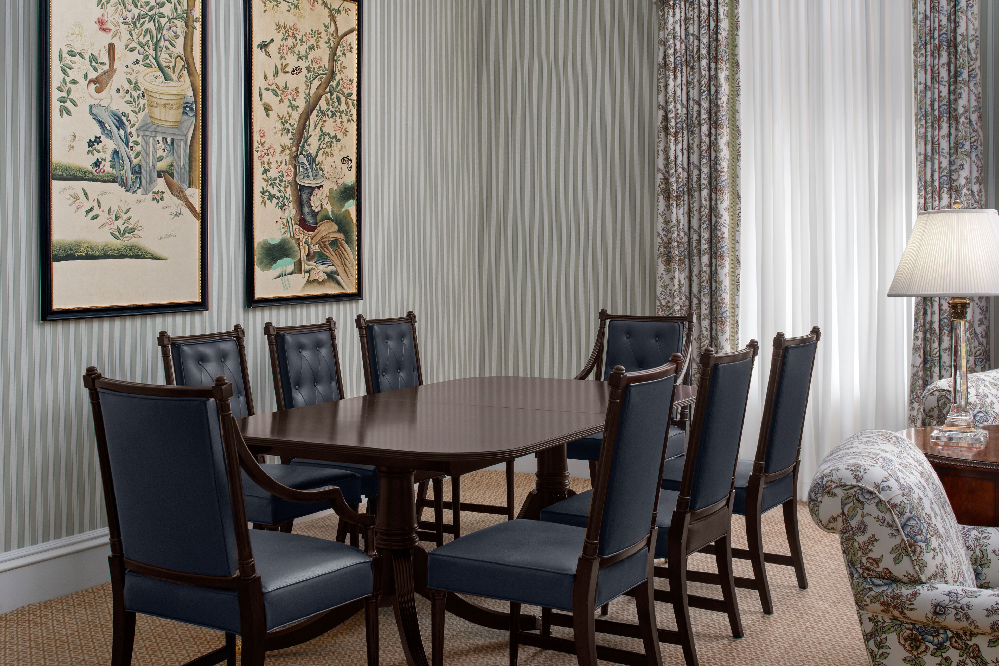 A dining room with a rectangular table surrounded by six chairs, flanked by two framed floral paintings.