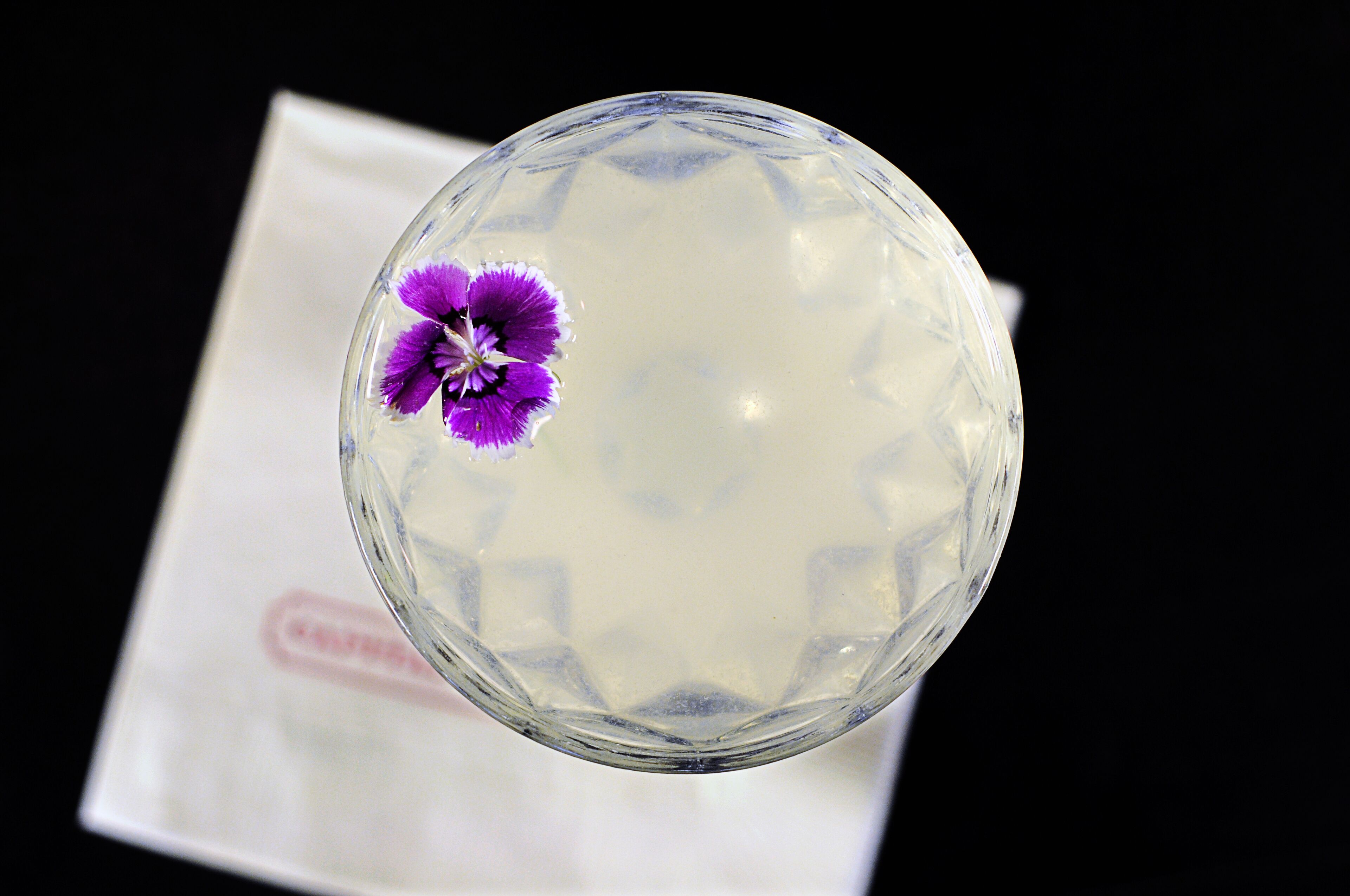 A clear glass with a purple flower on a white surface.