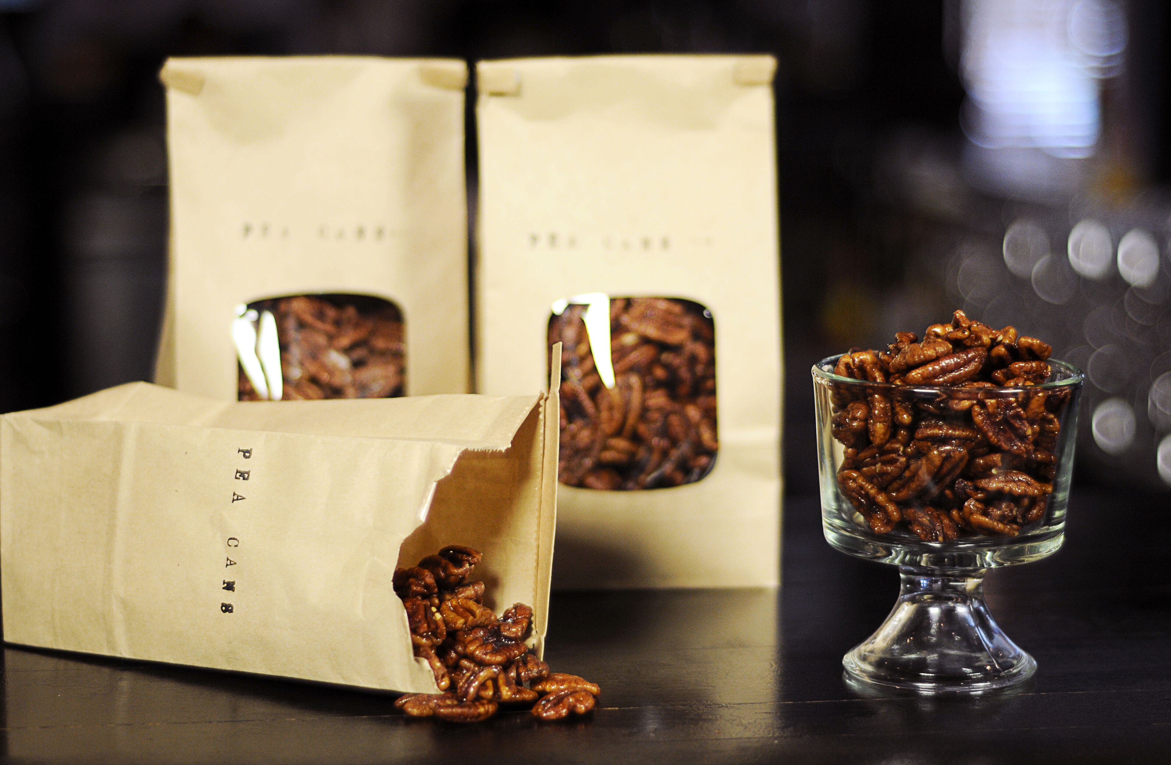 Una mesa con dos bolsas de papel etiquetadas "PEA CANNB" y un bol de vidrio lleno de nueces pecanas.