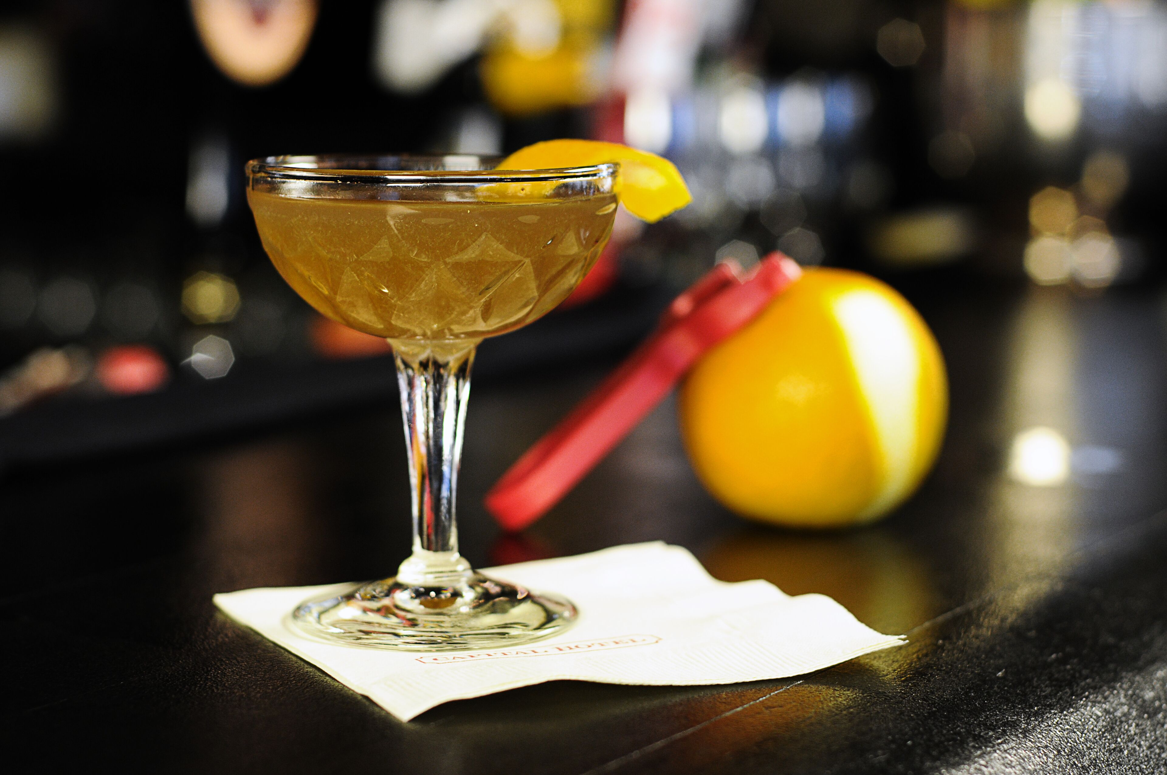 A cocktail in a martini glass with a lemon garnish on a bar counter.