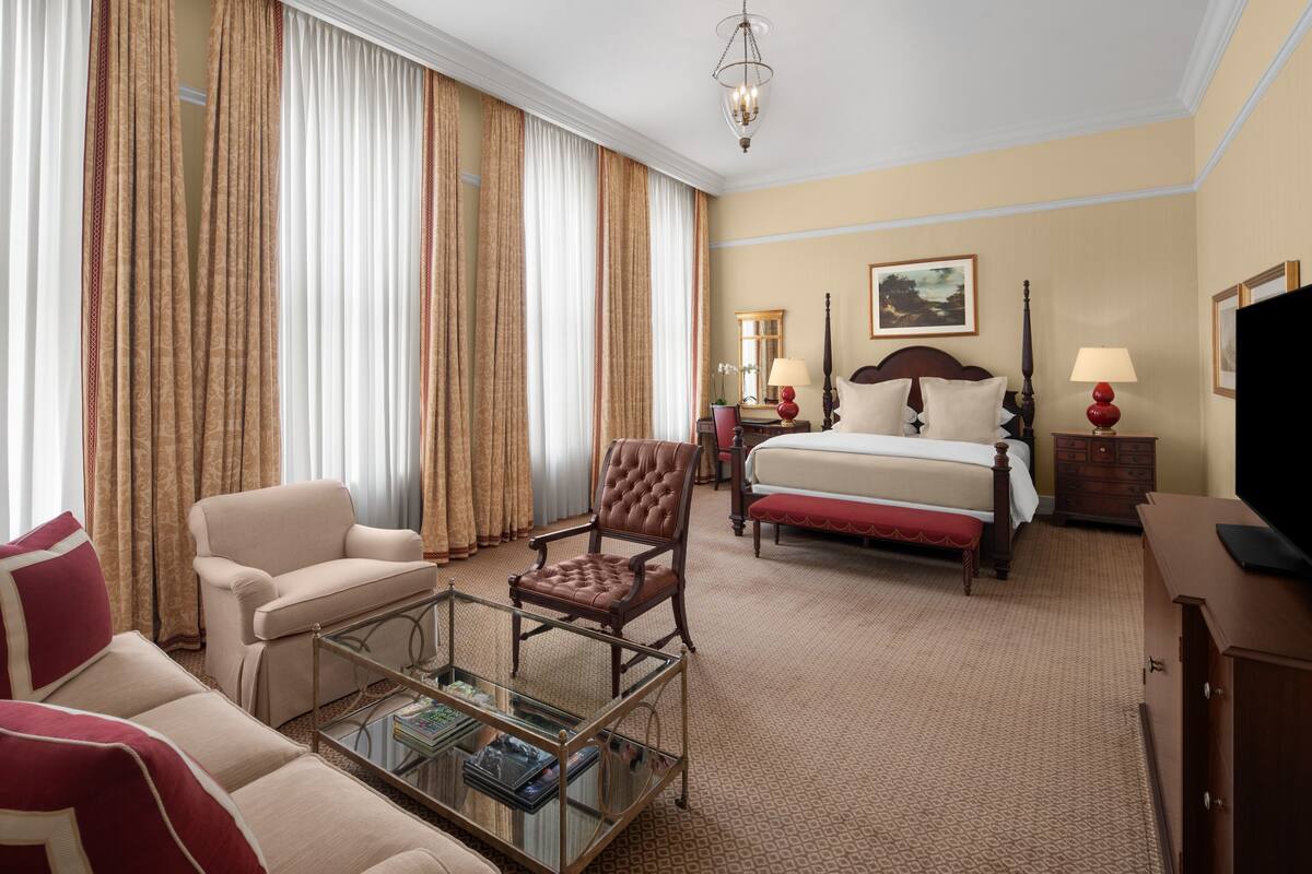 A hotel room with a bed, a sofa, a chair, a coffee table, a TV, and a dresser.