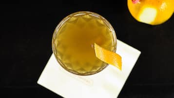 Un vaso de bebida color ámbar con una rodaja de limón sobre un paño blanco.