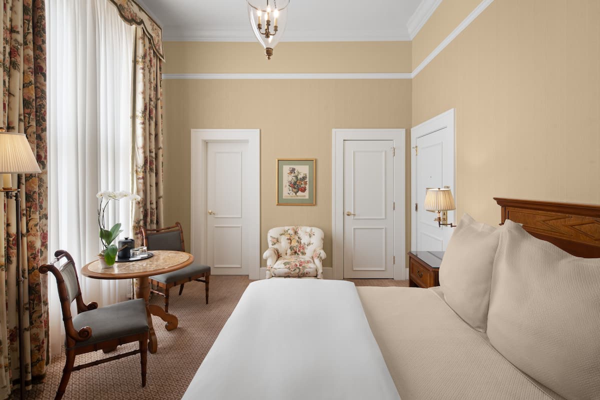 A hotel room with a bed, a chair, a table, and a lamp.