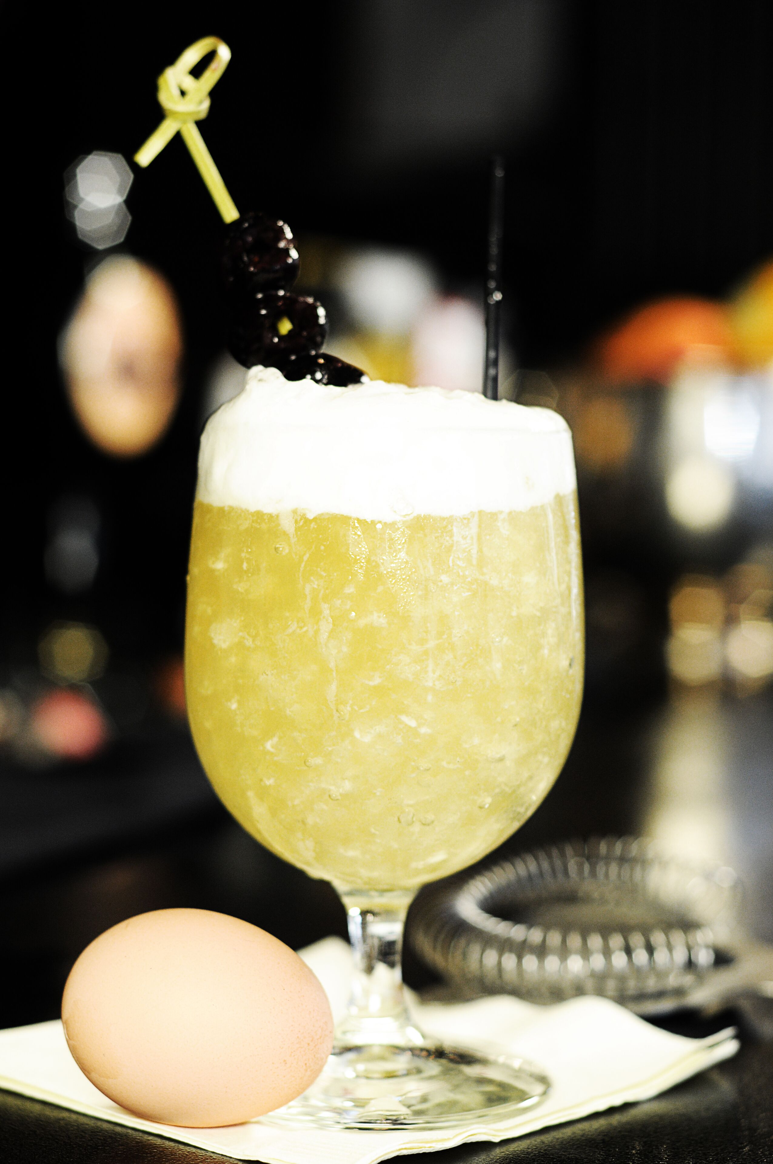 A cocktail glass with a garnish, an egg, and a cocktail shaker on a bar counter.
