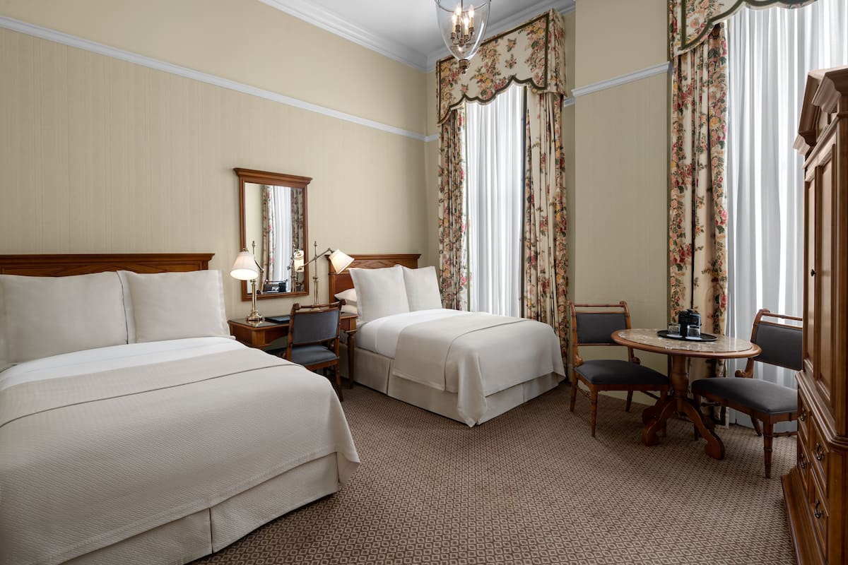 A hotel room with two beds, a desk, a chair, a small table, and a dresser.