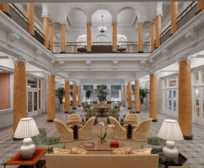 Un hall d’entrée spacieux, doté de hauts plafonds, de grandes colonnes et d’un espace de détente central avec de nombreux fauteuils et tables.